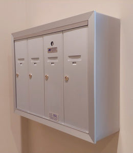 Surface mounted silver anodized aluminum vertical mailbox with four doors.