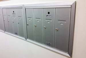 A recessed silver multi unit vertical mailbox with locks on the doors